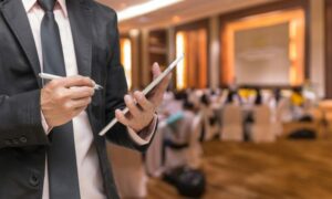 Homem com caderno na mão em um auditório para ilustrar texto de visita técnica